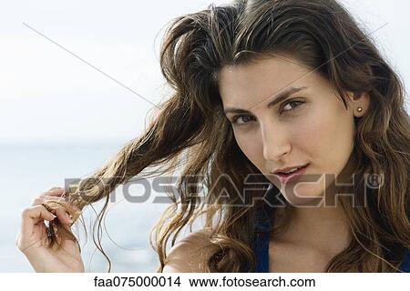 Young woman playing with ends of hair, smiling flirtatiously at camera View Large Photo Image Picture - Young woman playing with ends of hair, smiling flirtatiously at camera. Fotosearch