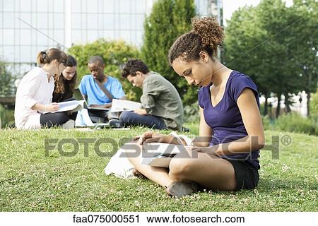Young woman reading book on grass, group of young people in background View Large Photo Image Stock Image - Young woman reading book on grass, group of young people in background. Fotosearch