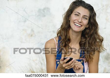Young woman text messaging, smiling at camera View Large Photo Image Stock Image - Young woman text messaging, smiling at camera. Fotosearch