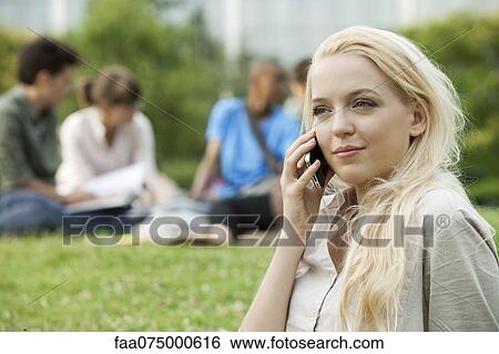 Stock Photograph - Young woman using cell phone, people in background, portrait. Fotosearch