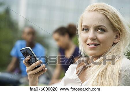Young woman with cell phone, people in background, portrait View Large Photo Image Stock Image - Young woman with cell phone, people in background, portrait. Fotosearch