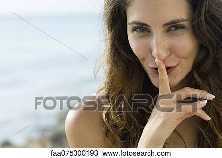 Stock Image - Young woman with finger on lips, portrait. Fotosearch