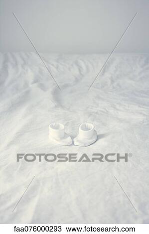 Stock Image - Baby booties on bed. Fotosearch