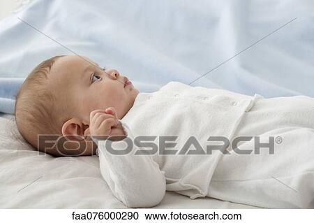 Stock Image - Baby boy lying on back, looking away attentively. Fotosearch