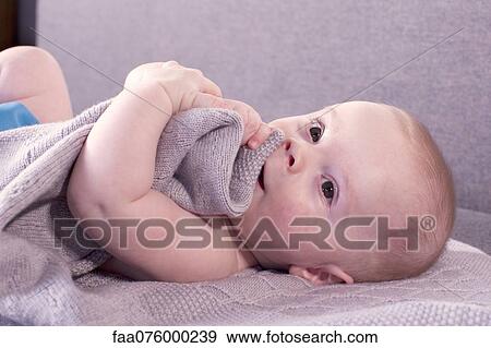 Stock Photo - Baby lying down, holding blanket. Fotosearch