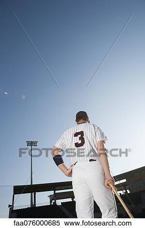 Stock Photography - Baseball player standing with hand on hip, rear view. Fotosearch