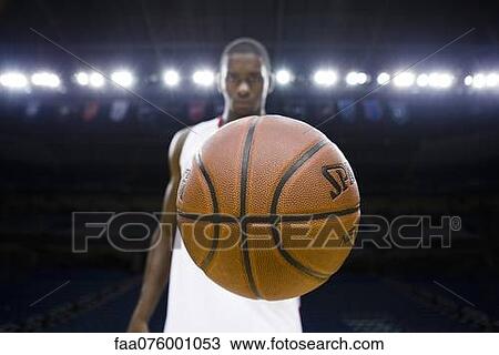 Stock Image - Basketball player holding basketball, focus on foreground. Fotosearch
