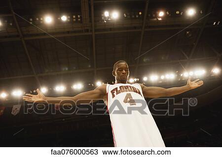 Stock Image - Basketball player standing with arms out, low angle view. Fotosearch