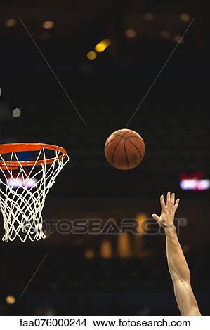 Picture - Basketball player throwing ball toward basketball hoop, cropped. Fotosearch