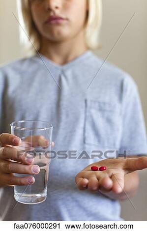 Boy holding glass of water and tablets, mid section View Large Photo Image Stock Image - Boy holding glass of water and tablets, mid section. Fotosearch