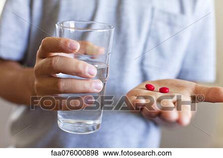 Stock Photo - Boy holding glass of water and tablets, cropped. Fotosearch