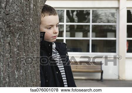 Stock Photo - Boy leaning against tree trunk. Fotosearch