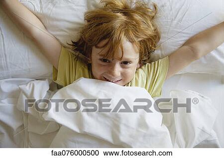 Stock Image - Boy lying in bed with arms outstretched. Fotosearch