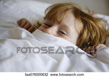 Stock Image - Boy lying in bed with bed sheet covering face. Fotosearch