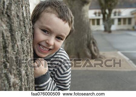 Stock Photo - Boy peeking from behind tree, portrait. Fotosearch