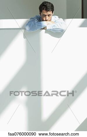 Stock Image - Businessman leaning against balcony with head resting on arms. Fotosearch