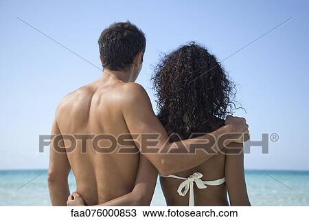 Couple at the beach, looking at sea, rear view View Large Photo Image Stock Image - Couple at the beach, looking at sea, rear view. Fotosearch
