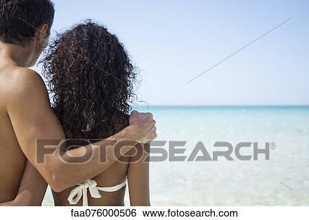 Couple at the beach, looking at sea, rear view View Large Photo Image Stock Photograph - Couple at the beach, looking at sea, rear view. Fotosearch