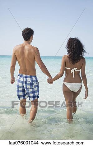 Couple holding hands while wading in sea, rear view View Large Photo Image Picture - Couple holding hands while wading in sea, rear view. Fotosearch