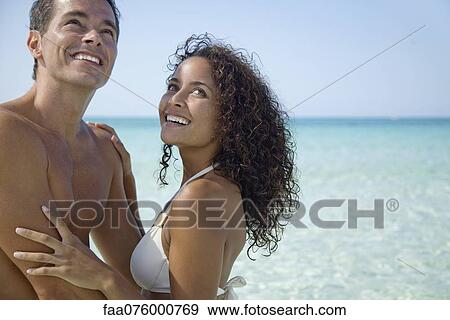Stock Photo - Couple together at the beach, looking up and smiling. Fotosearch
