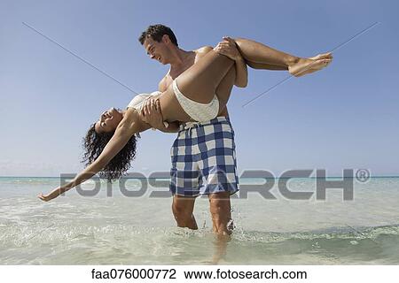 Couple together at the beach, man carrying woman in water View Large Photo Image Stock Image - Couple together at the beach, man carrying woman in water. Fotosearch