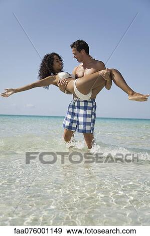 Stock Photo - Couple together at the beach, man carrying woman. Fotosearch