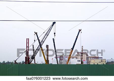 Stock Image - Cranes behind corrugated metal fence. Fotosearch