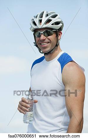 Stock Image - Cyclist holding water bottle, portrait. Fotosearch
