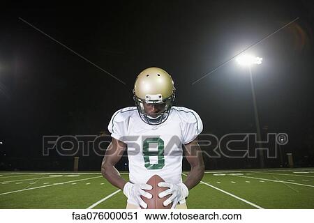 Stock Image - Football player holding ball, head down in concentration. Fotosearch