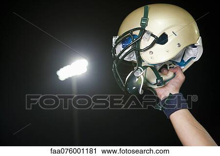 Stock Image - Football player holding up helmet in victory, cropped. Fotosearch