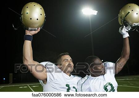 Stock Photograph - Football players holding up helmets in victory. Fotosearch