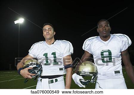 Stock Photo - Football players standing side by side, holding helmets. Fotosearch