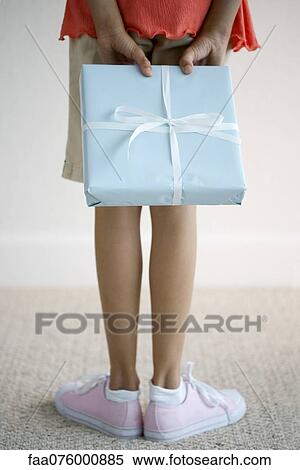 Stock Photography - Girl holding gift behind back, low section. Fotosearch