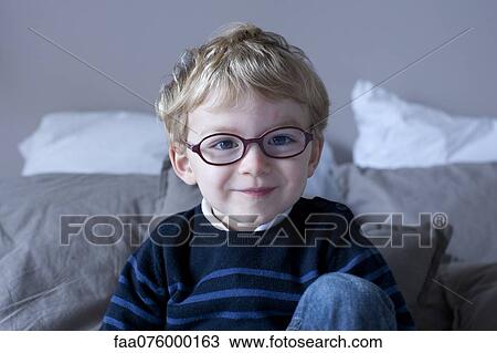 Stock Image - Little boy sitting on bed, portrait. Fotosearch