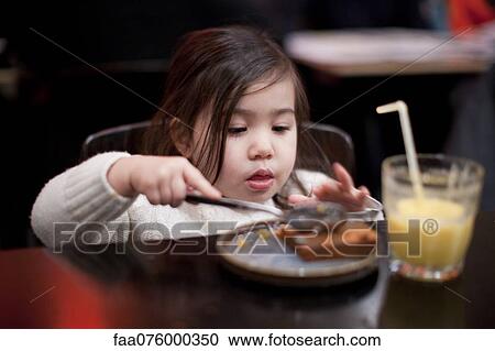 Stock Image - Little girl eating at table. Fotosearch