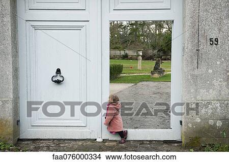 Picture - Little girl leaning against open door, looking into courtyard. Fotosearch