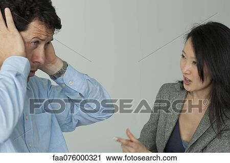 Stock Image - Man and woman arguing, man covering his ears with hands. Fotosearch