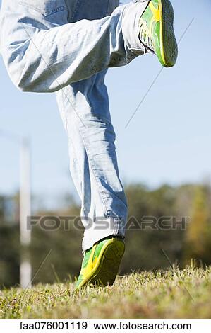 Stock Photo - Man in jeans running on grass, low section. Fotosearch