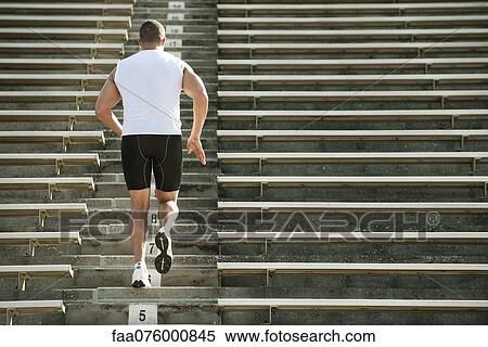 Stock Photography - Man running up steps in stadium, rear view. Fotosearch