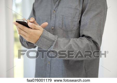 Stock Photo - Man using smartphone, mid section. Fotosearch