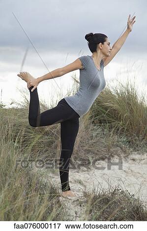 Stock Photo - Mature woman in Natarajasana pose on beach, side view. Fotosearch