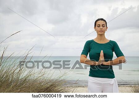 Stock Photo - Mature woman in prayer position on beach, portrait. Fotosearch