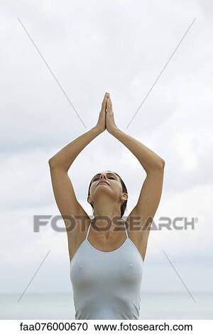 Stock Image - Mature woman in prayer position with arms above head. Fotosearch