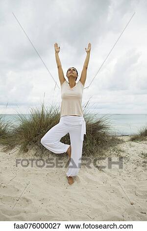 Stock Photo - Mature woman in tree pose on beach, portrait. Fotosearch