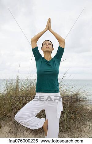 Stock Photography - Mature woman in tree pose on beach, portrait. Fotosearch