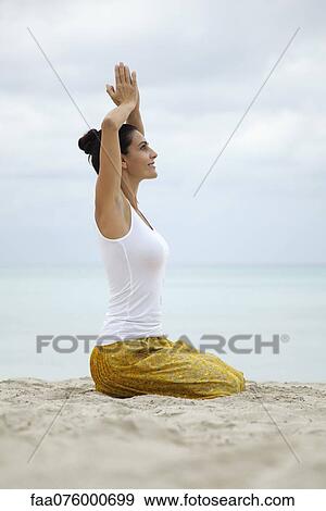 Stock Photo - Mature woman kneeling in prayer position with hands above head, side view. Fotosearch