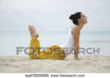 Stock Photo - Mature woman practicing yoga on beach, side view. Fotosearch
