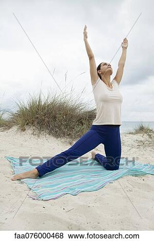Stock Photo - Mature woman practicing yoga on beach. Fotosearch
