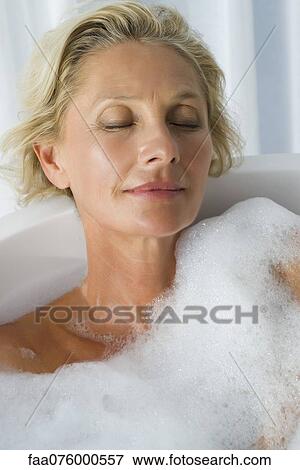 Stock Photo - Mature woman relaxing in bubble bath with eyes closed, portrait. Fotosearch