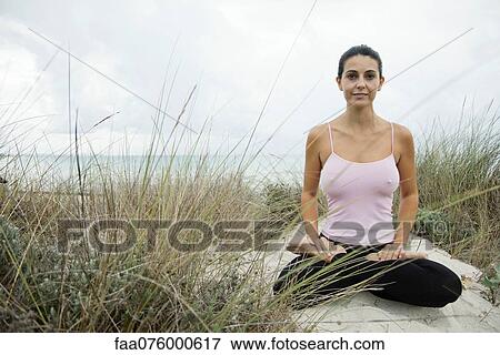 Stock Photo - Mature woman sitting in lotus position on beach, portrait. Fotosearch